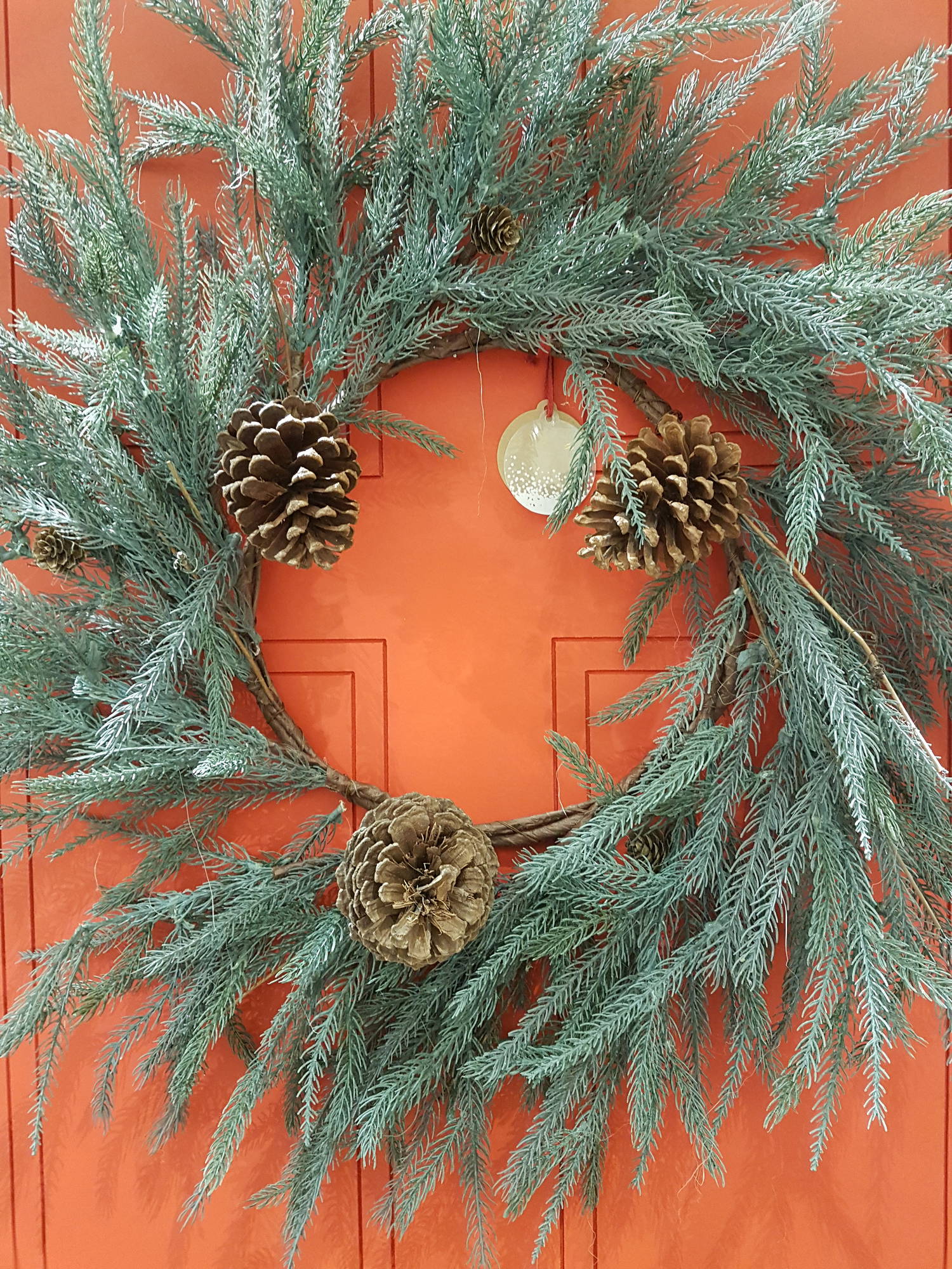 Red door decorated with Christmas wreath of pine branches and pine cones